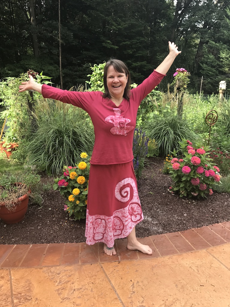 Gail with her arms out in front of flowers wearing a Spinning Babies© red dress